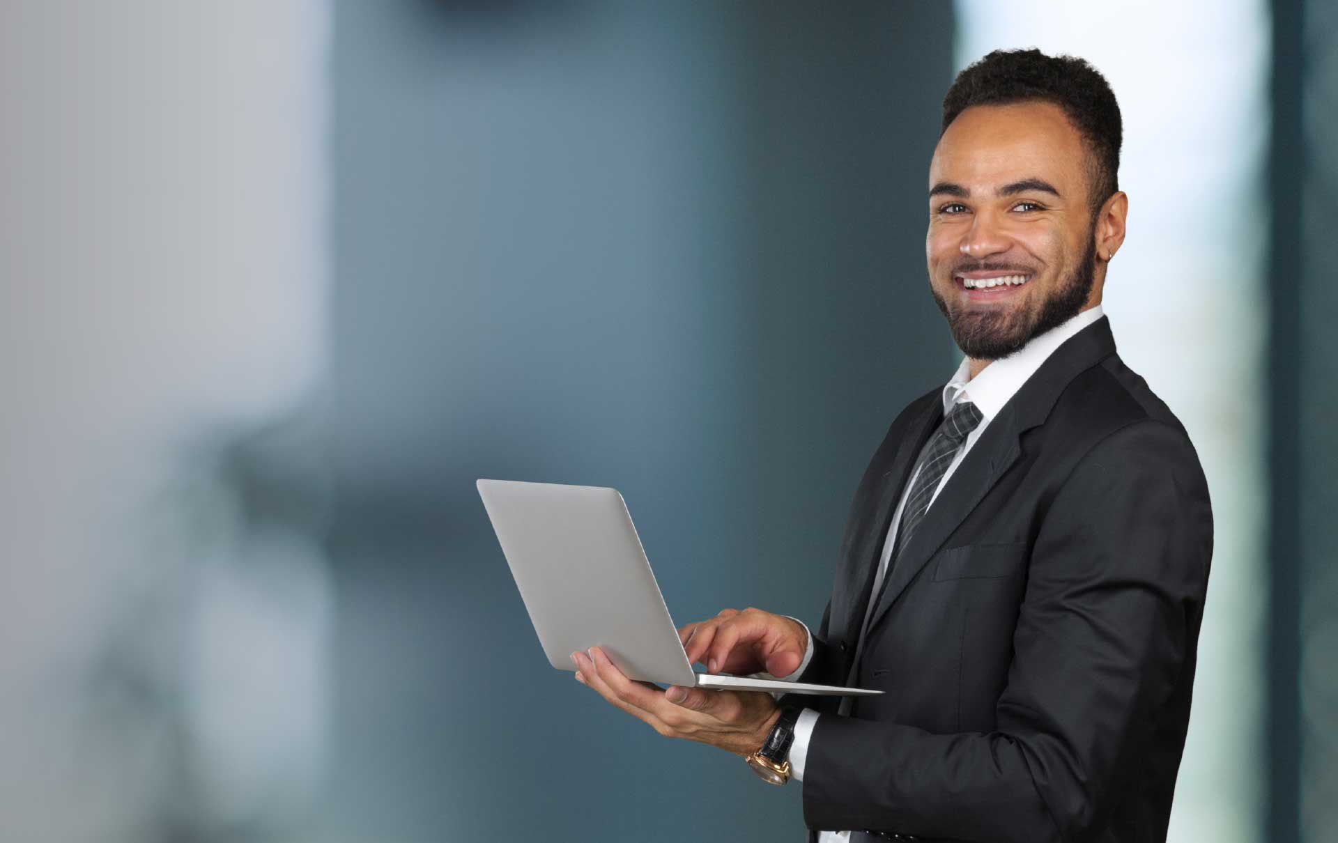 Professional business executive wearing a black suit, working on his laptop and smiling.